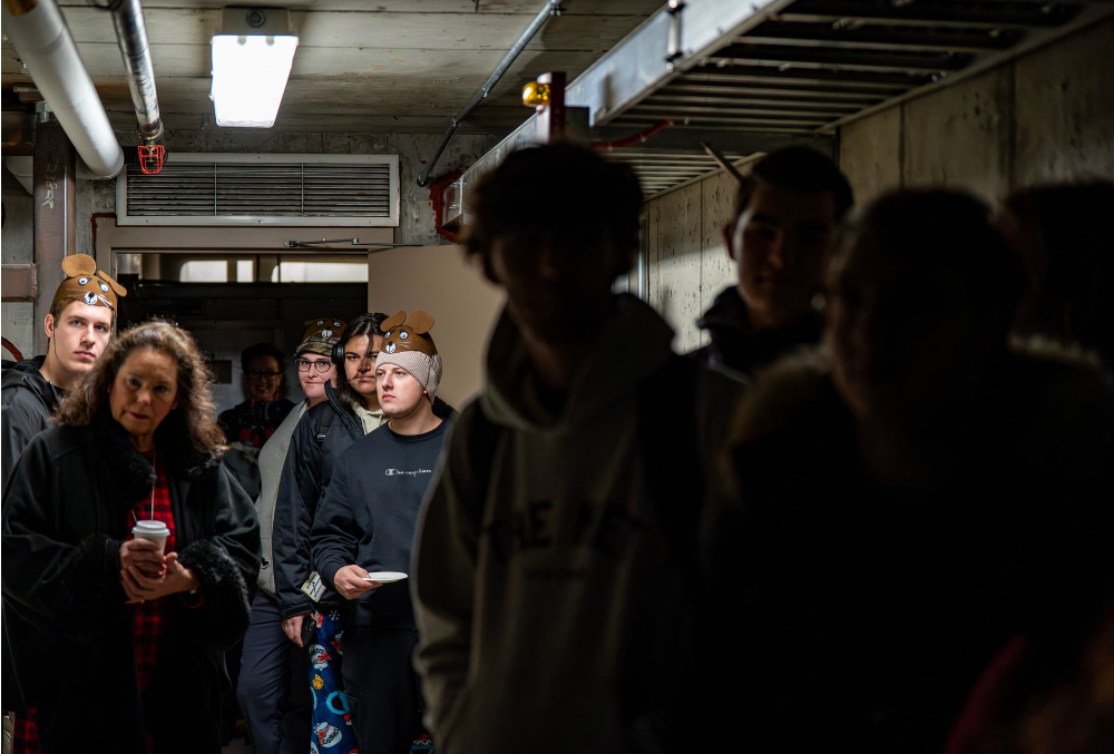 people walking through a tunnel with overhead lights, right side of photo darker