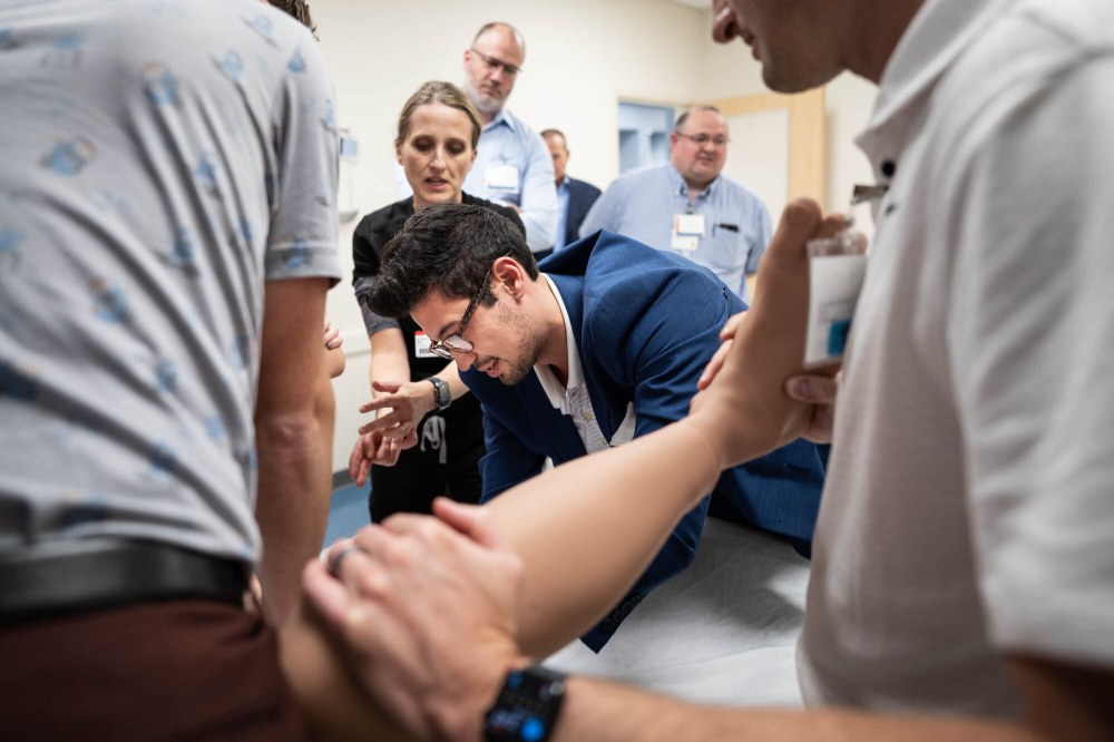 group of health care providers crowd around a pregnant mannequin, learning how to deliver a baby whose shoulders are stuck