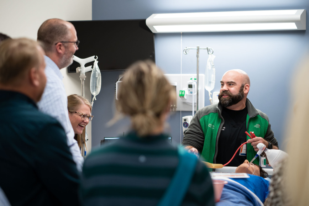 a mannequin with air tubes is in a bed while four people look on during a demonstration