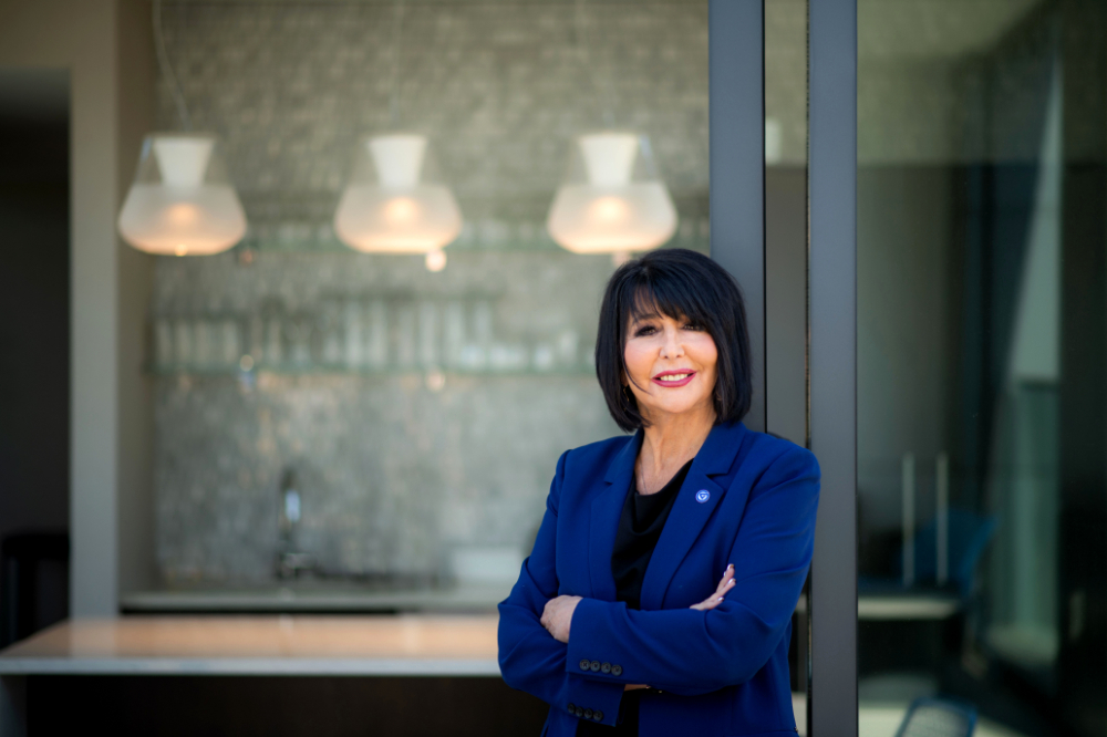 President Mantella in blue jacket with arms crossed in front of wall with three lights in background