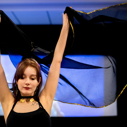 student with arms raised doing belly dance holding sheer fabric over her head