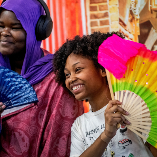two young students hold colorful fans while posing with photo booth props