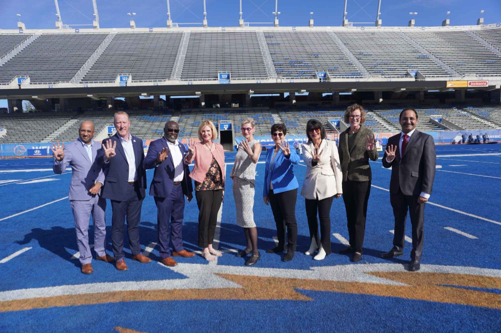 nine people on a football field with blue turf holding their hands out showing the number four
