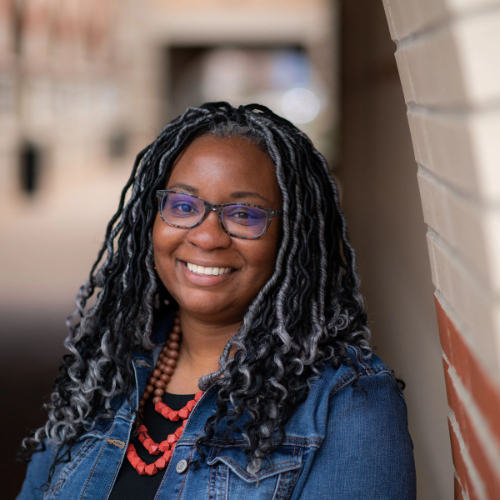 Laila McCloud, assistant professor of educational leadership and counseling, standing outside the DeVos Center wearing a denim shirt and red necklace