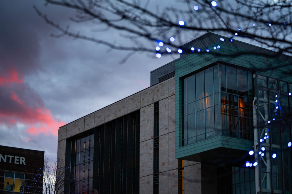 the sun sets on the Mary Idema Pew Library, the tree in the foreground is lit with white lights