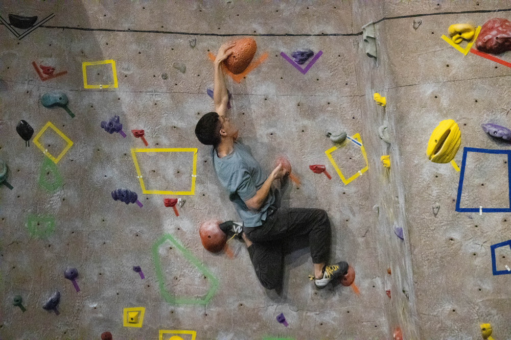 colorful climbing wall, one person reaching for rock with left hand, feet gripping rocks