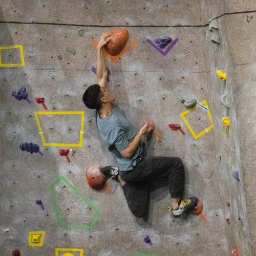 colorful climbing wall, one person reaching for rock with left hand, feet gripping rocks