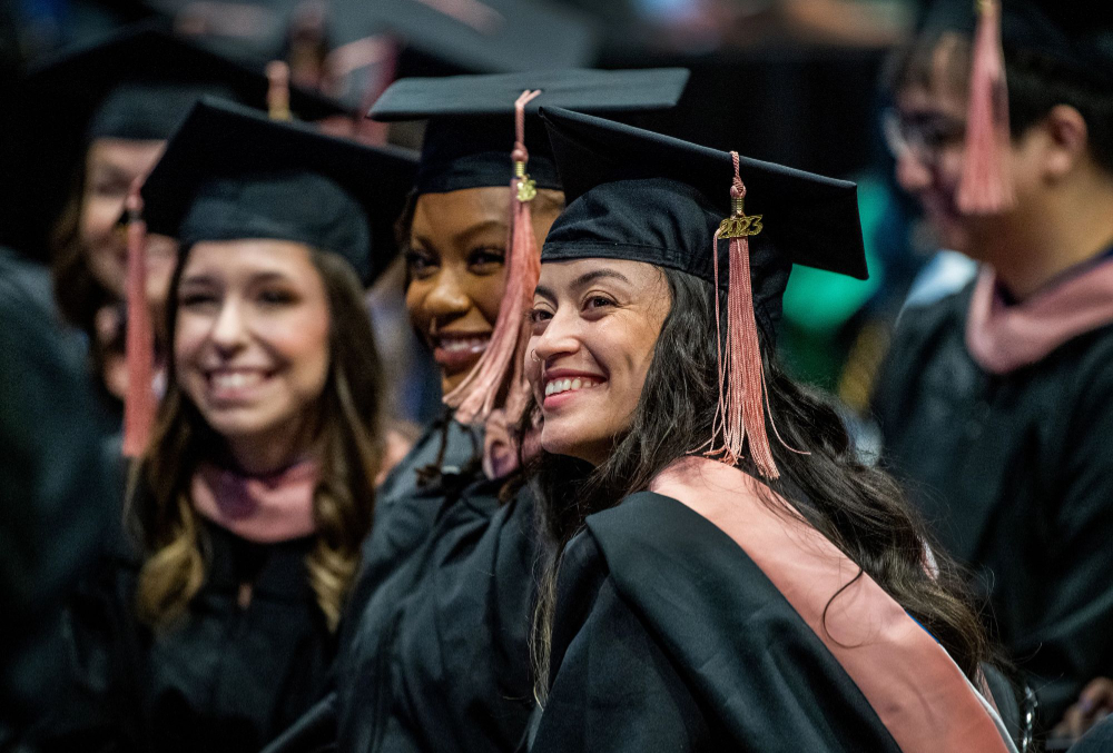 smiling graduates in black gowns with salmon colored stoles