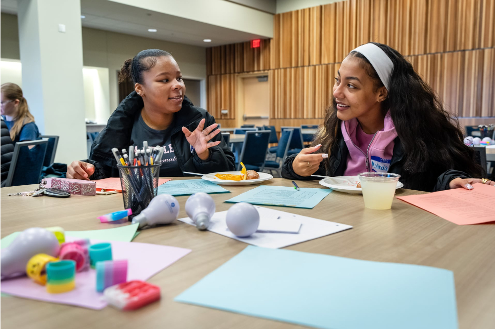 two students seated at table with crafting supplies in front of them