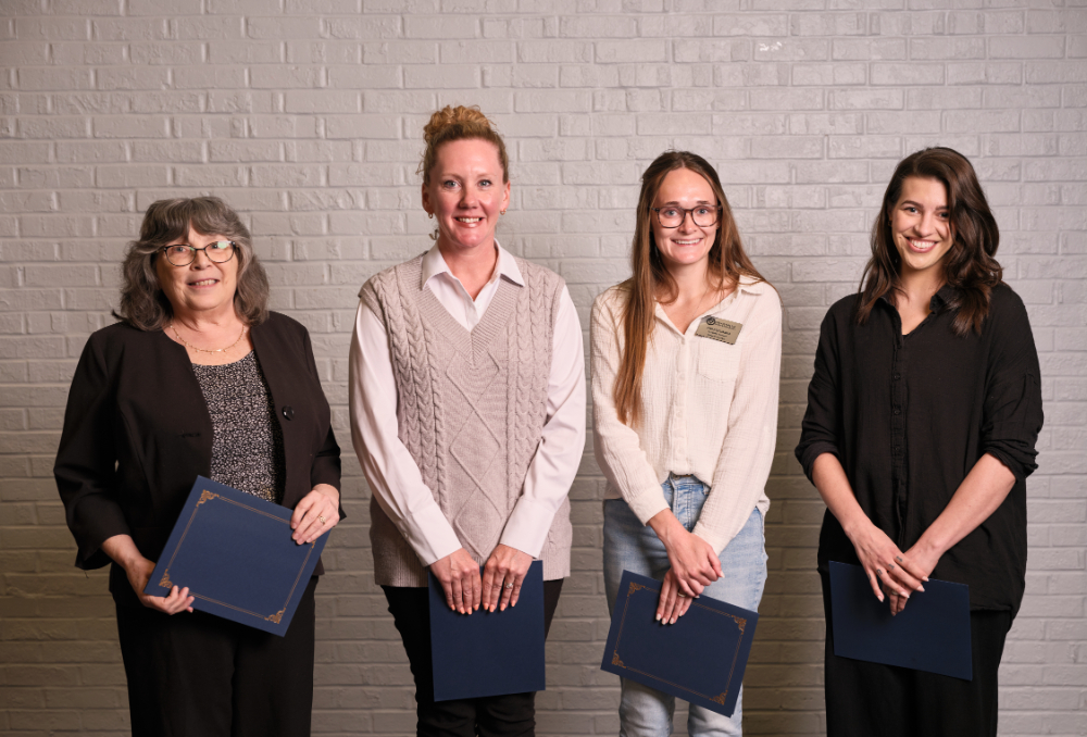 four people against a wall, holding certificates