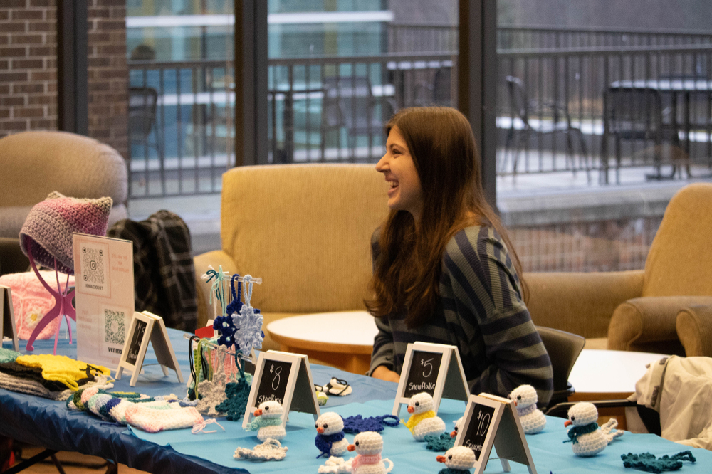 student sits behind table of small crocheted items at a craft fair