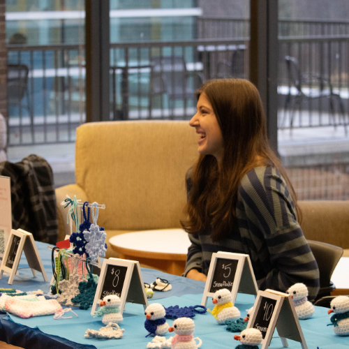 student sits behind table of small crocheted items at a craft fair
