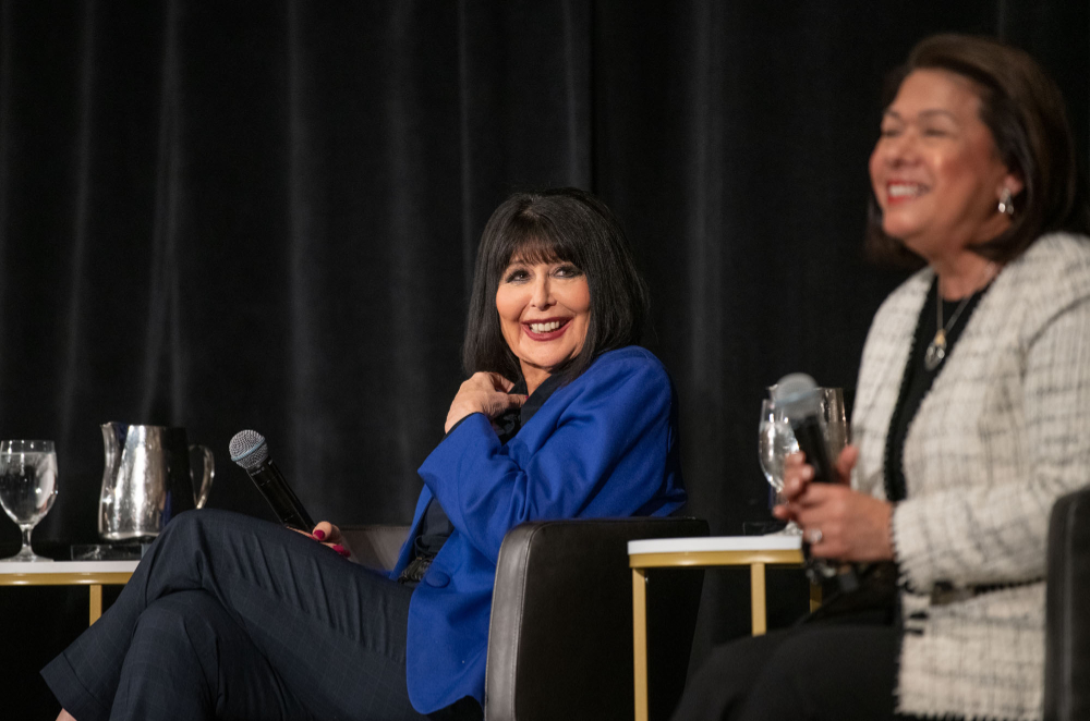 President Mantella smiles at woman to her left while on stage during a panel discussion