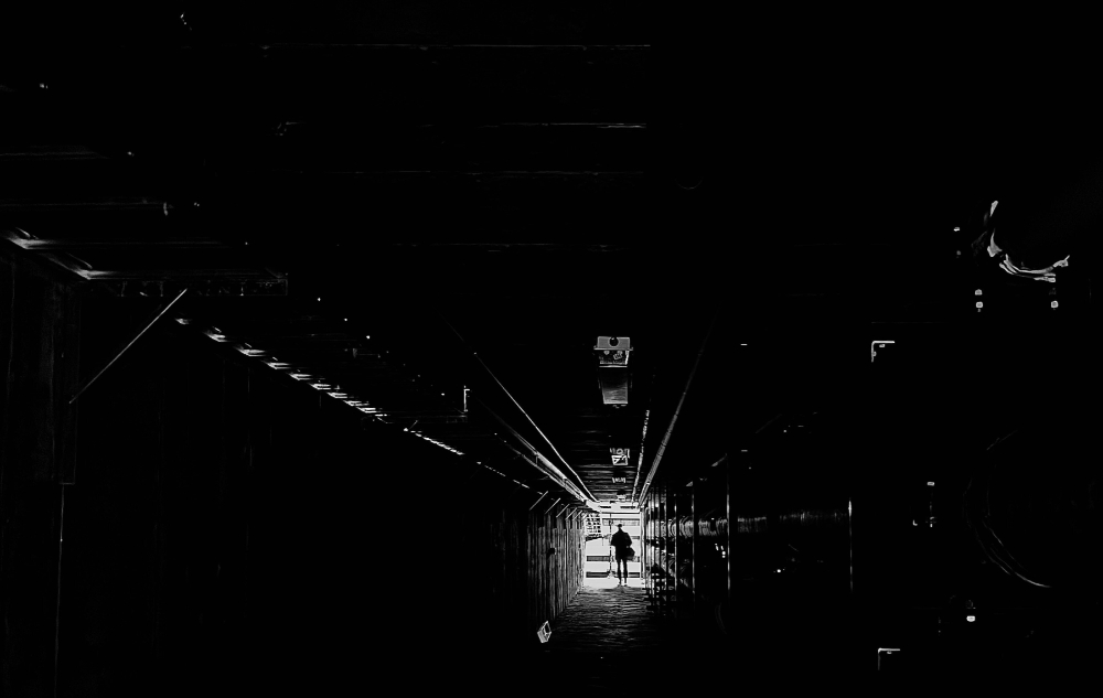 person at end of tunnel under Lake Ontario Hall lit by light, otherwise black tunnel