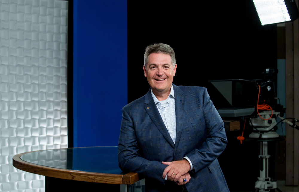 Jim Rademaker, WGVU general manager, standing next to desk at TV studio