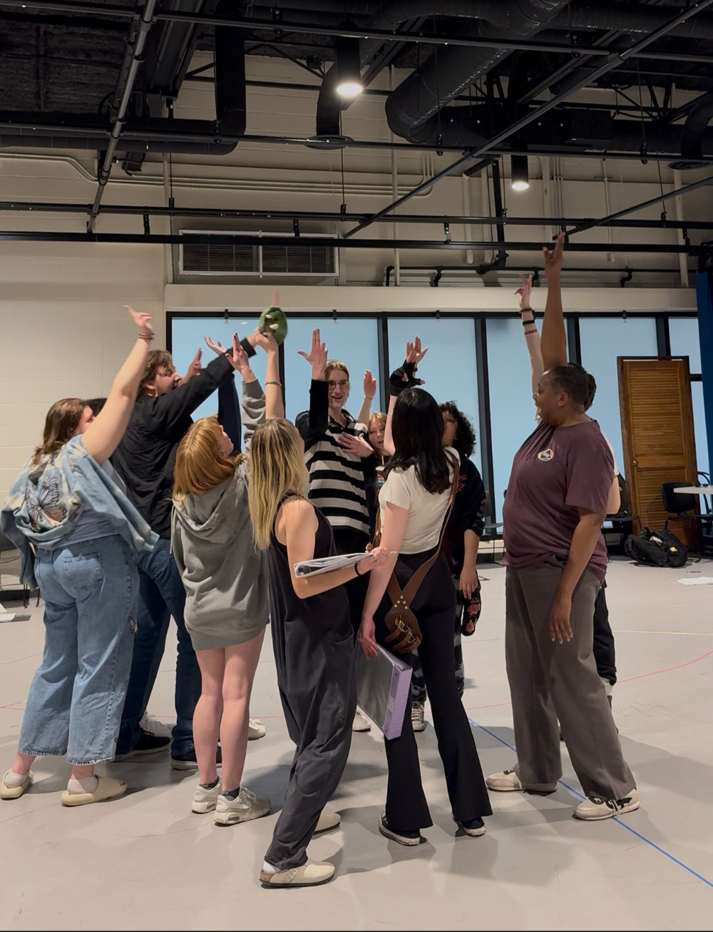 students in loose circle standing and raising hands to the center of circle