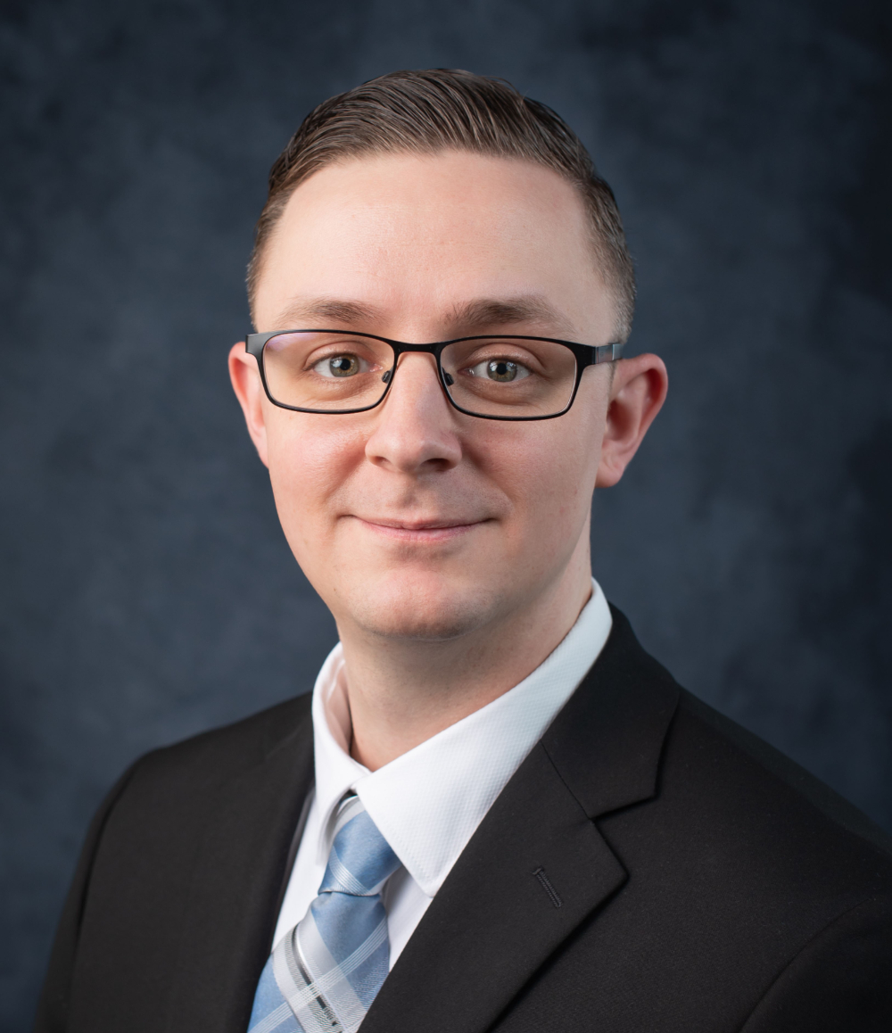 Matt Showalter in dark suit jacket and white shirt, wearing glasses