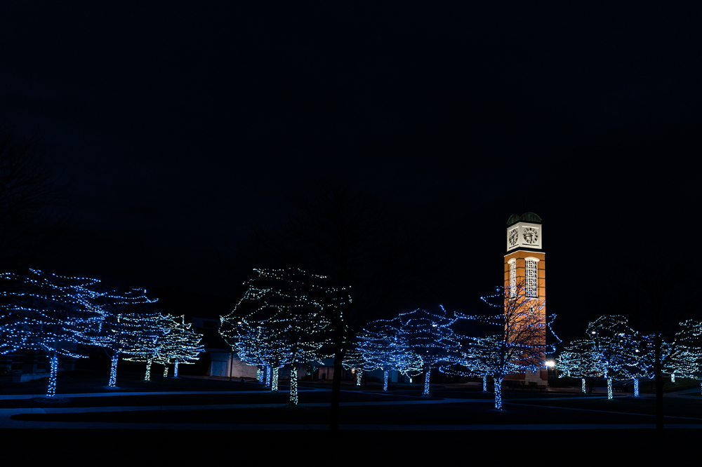 Cook Carillon Tower at night with trees in front decorated with holiday blue lights