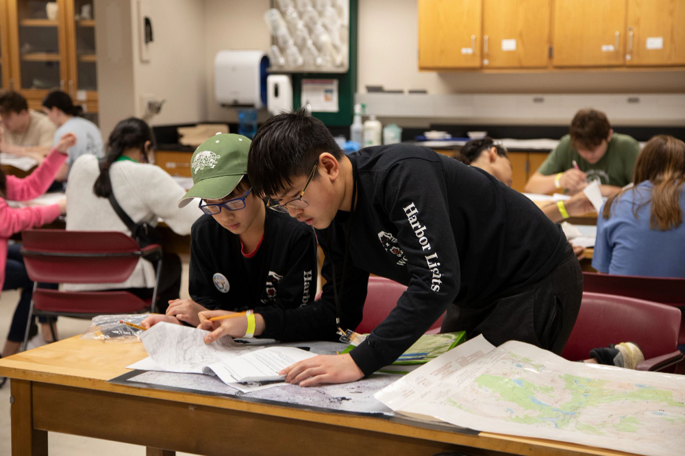 two people leaning over table with paperwork spread out on long table