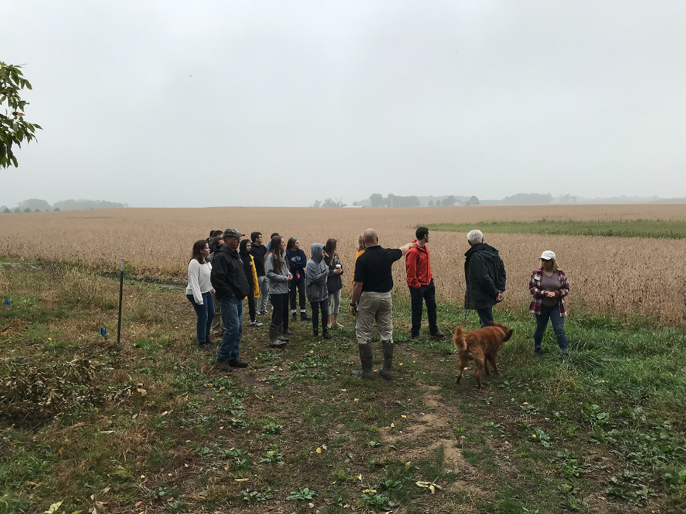group of people looking at a farm field, man is pointing at the field