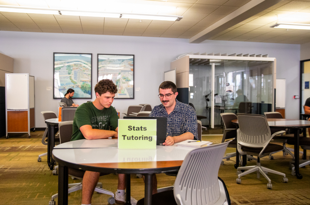 two people at table, with sign Stats Tutoring in front