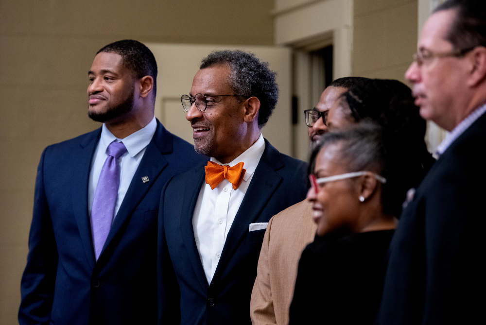 in profile are six people looking forward at another camera; photo taken from stage right