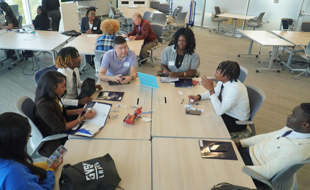 four tables pushed together to make large rectangle table with students and faculty seated around
