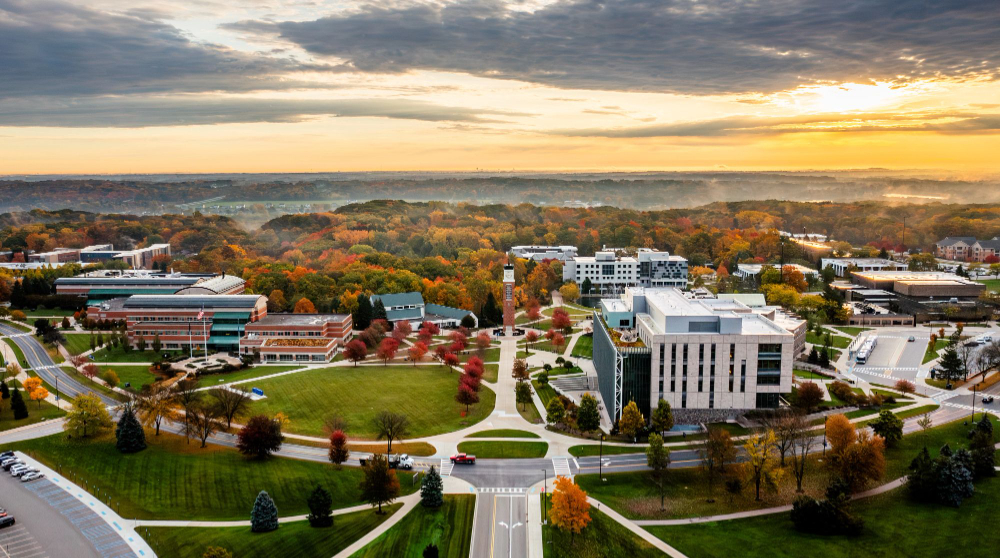 drone photo of Allendale Campus with sidewalk to clock tower and tour in center; autumn leaves on trees and sunset in background