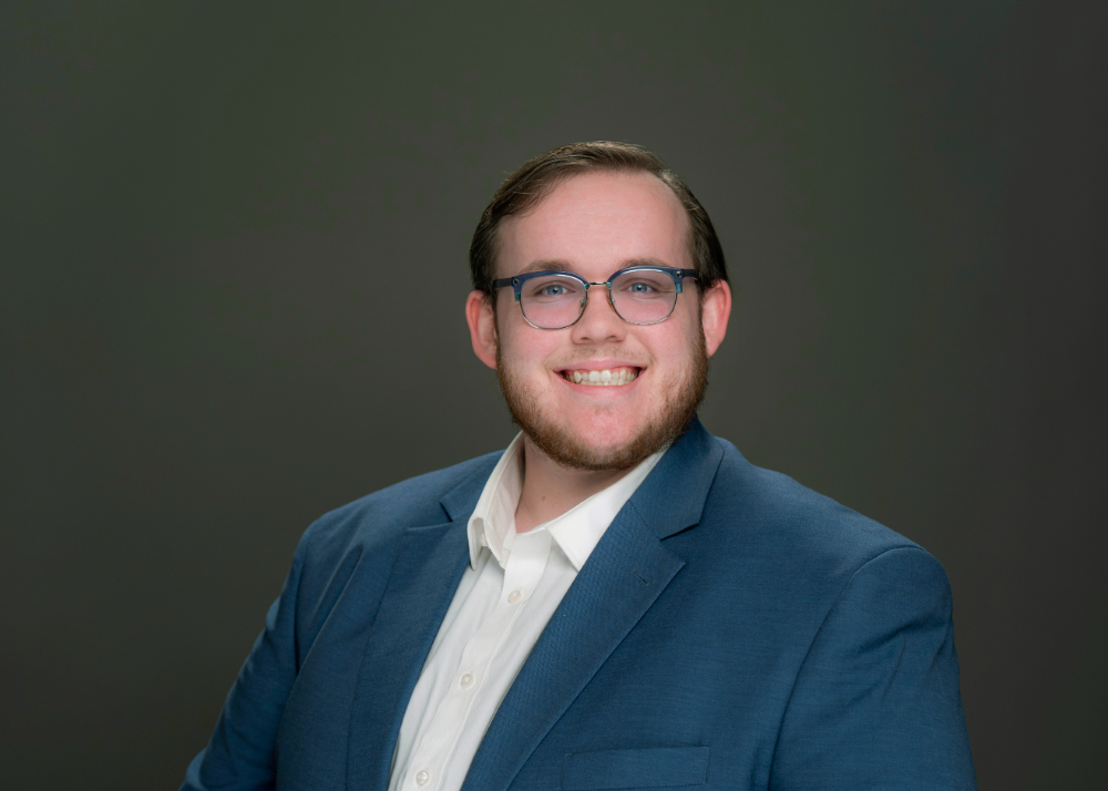 Ben Robar seated for portrait in blue jacket and white shirt