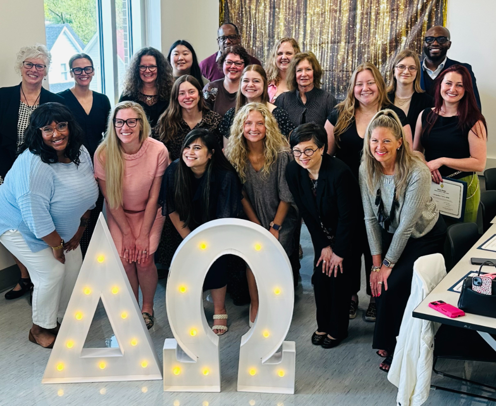 large group of people standing behind Delta Omega letters with lights inside them