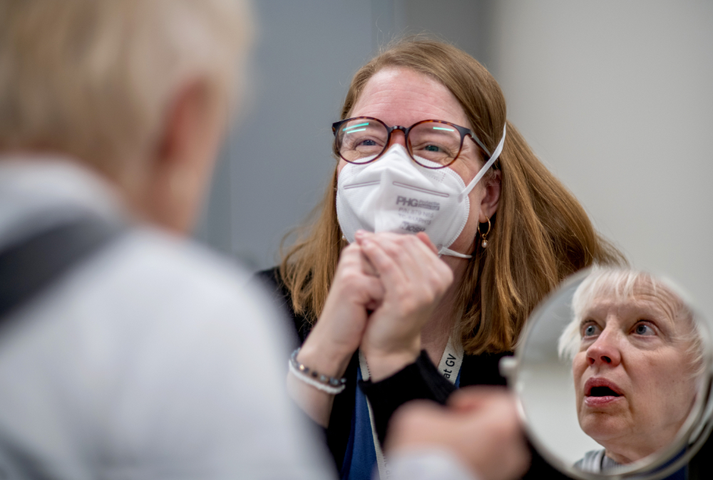 woman in mask tests the hearing of another person, whose face you only see in a mirror