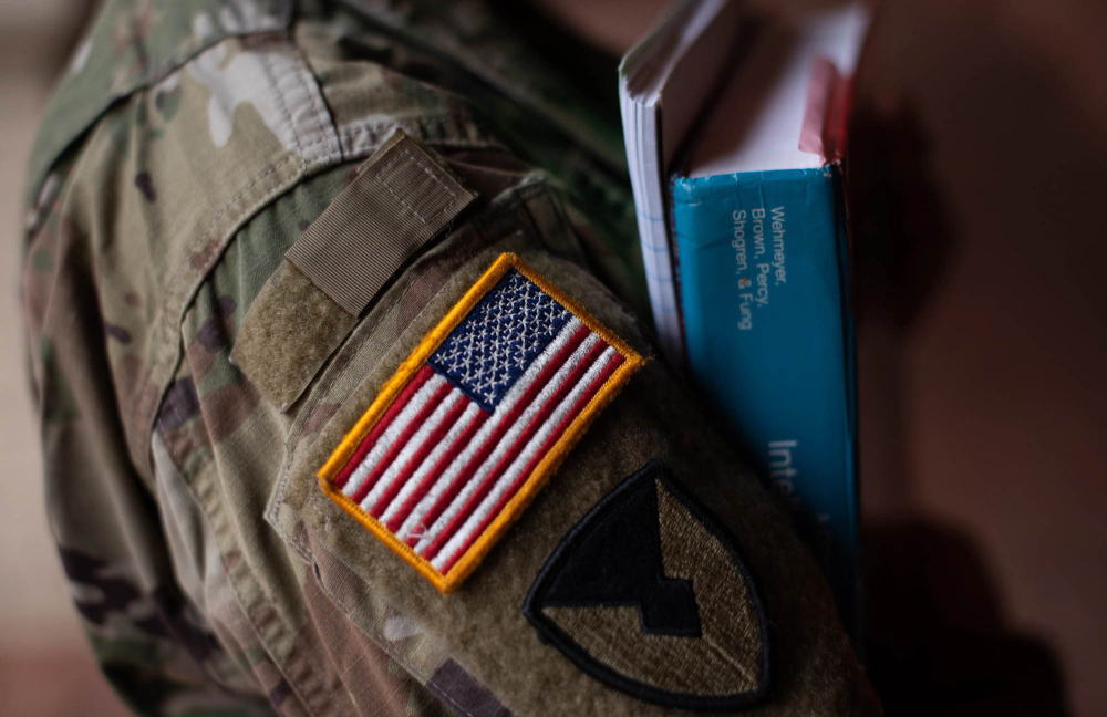 close up photo of military camoflauge sleeve with US flag, arms holding textbooks