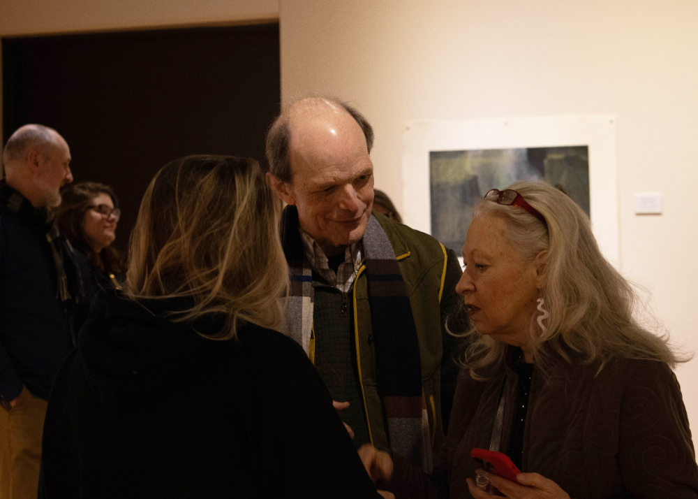 small group talking in an art gallery, three people in forefront in front of artwork on wall