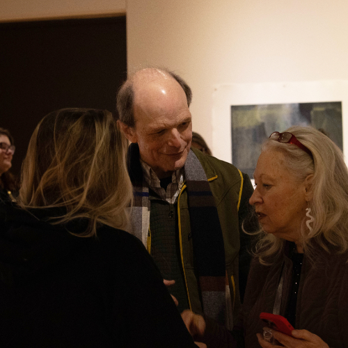 small group talking in an art gallery, three people in forefront in front of artwork on wall