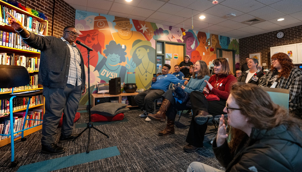 DL McKinney stands with right arm outstretched, people gathered for an event seated in chairs in front