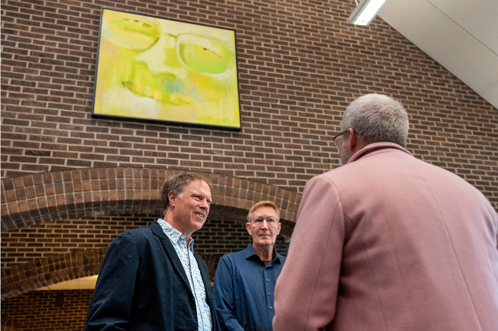 two people standing under yellow painting, talking to man in overcoat