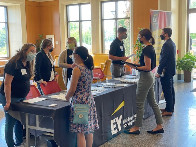people standing on either side of a long table, draped with EY banner, at an accounting recruitment event