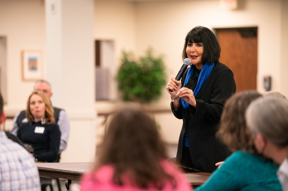 President Mantella stands with microphone to address people seated at tables around her