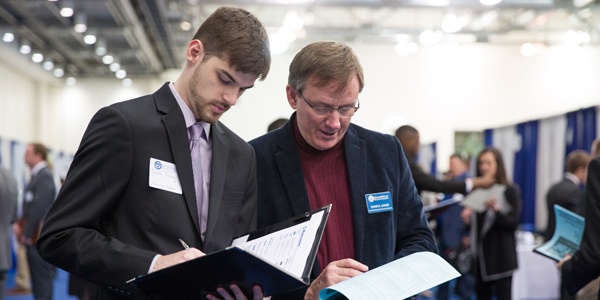 Student at career fair taking notes while speaking with an employee recruiter.