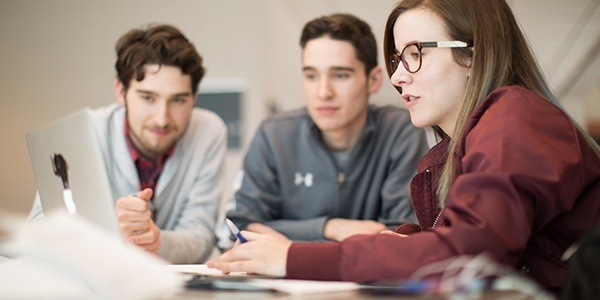 three students sitting around a laptop.