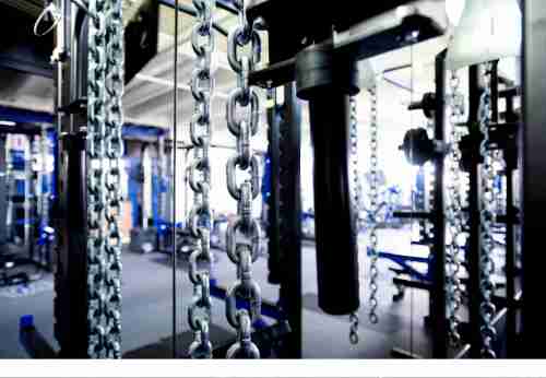An artistic shot of a gym space including weight lifting equipment and chains is shown.