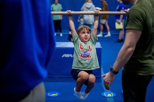 A small child holds onto a bar and looks up. The arms of two grand valley students are frame the image in the foreground.