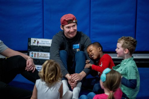 Small children gather around a GVSU student wearing a red hat. One child is holding onto his arm.