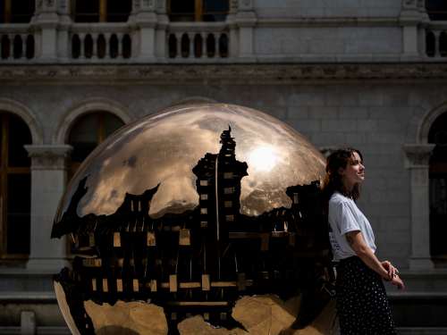A student leans her back against a copper globe sculpture that is 7-8 feet tall.