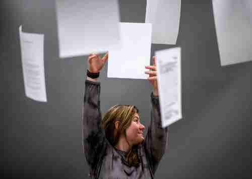 A person reaches for paper hanging from the ceiling. This behind the scenes photo shows the scene with no special moody lighting. 