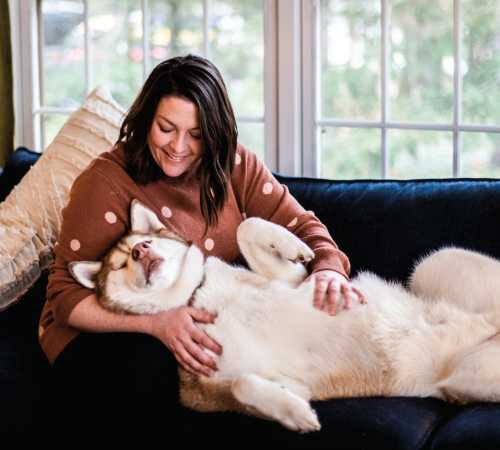 Stephanie Aikens sits on her couch while her dog lays on her lap