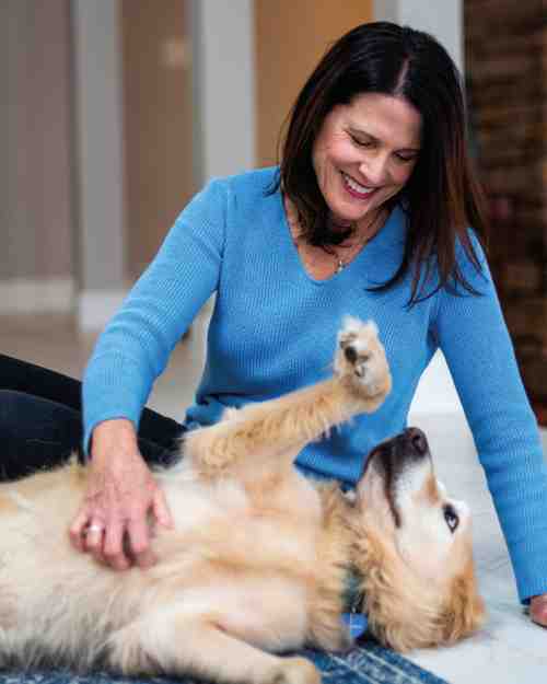 Mary Eilleen sits on the floor next to her dog and rubs their chest