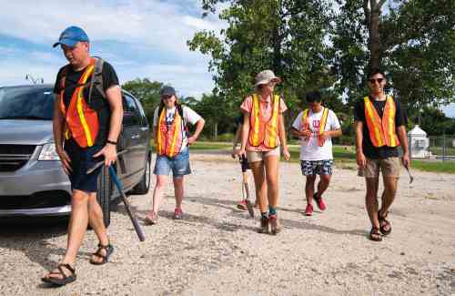 A group of 5 students walk across a parking lot wearing high vis vests