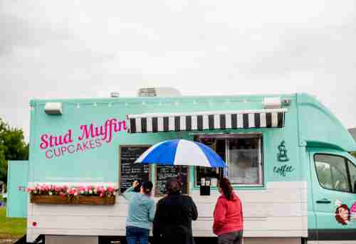 People under umbrellas line up at the teal and white Stud Muffin truck