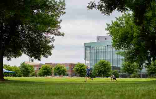 A runner participating in the 5k runs across campus with the library and kirkhof in the distance